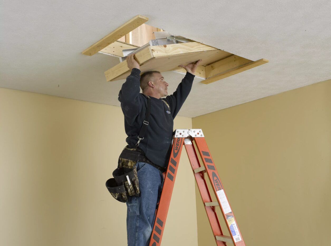 A handyman installs an attic ladder