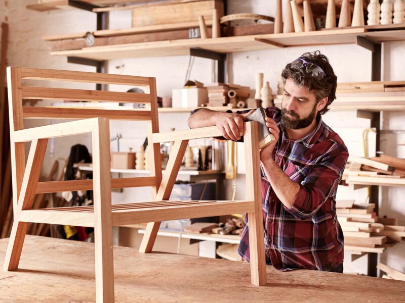 Furniture designer sanding a wooden chair frame